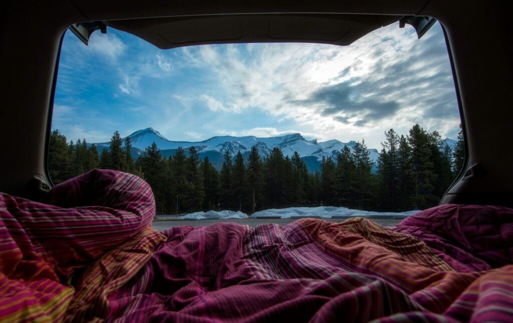 Cozy budget micro camper setup in the back of a car looking out at mountains.